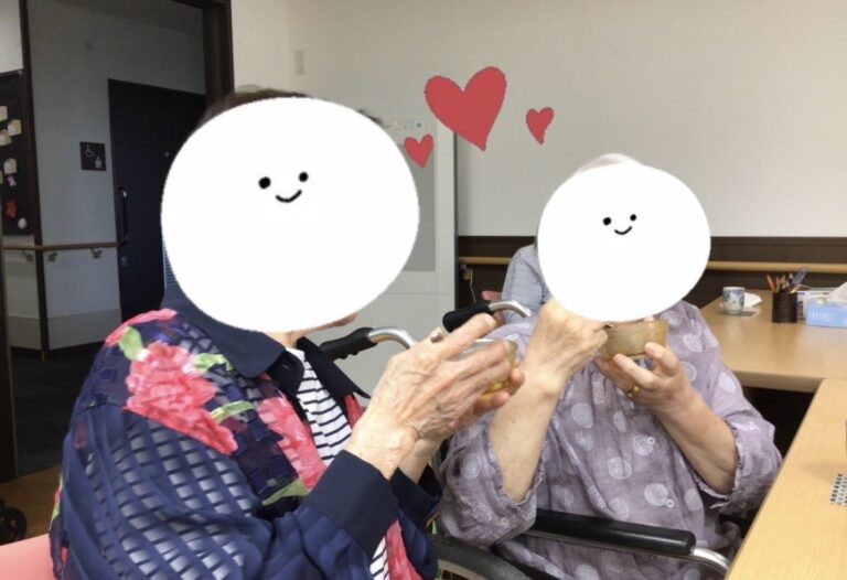 入居者2名が手をつなぎ、笑顔で交流する様子。壁にはハート装飾がある。