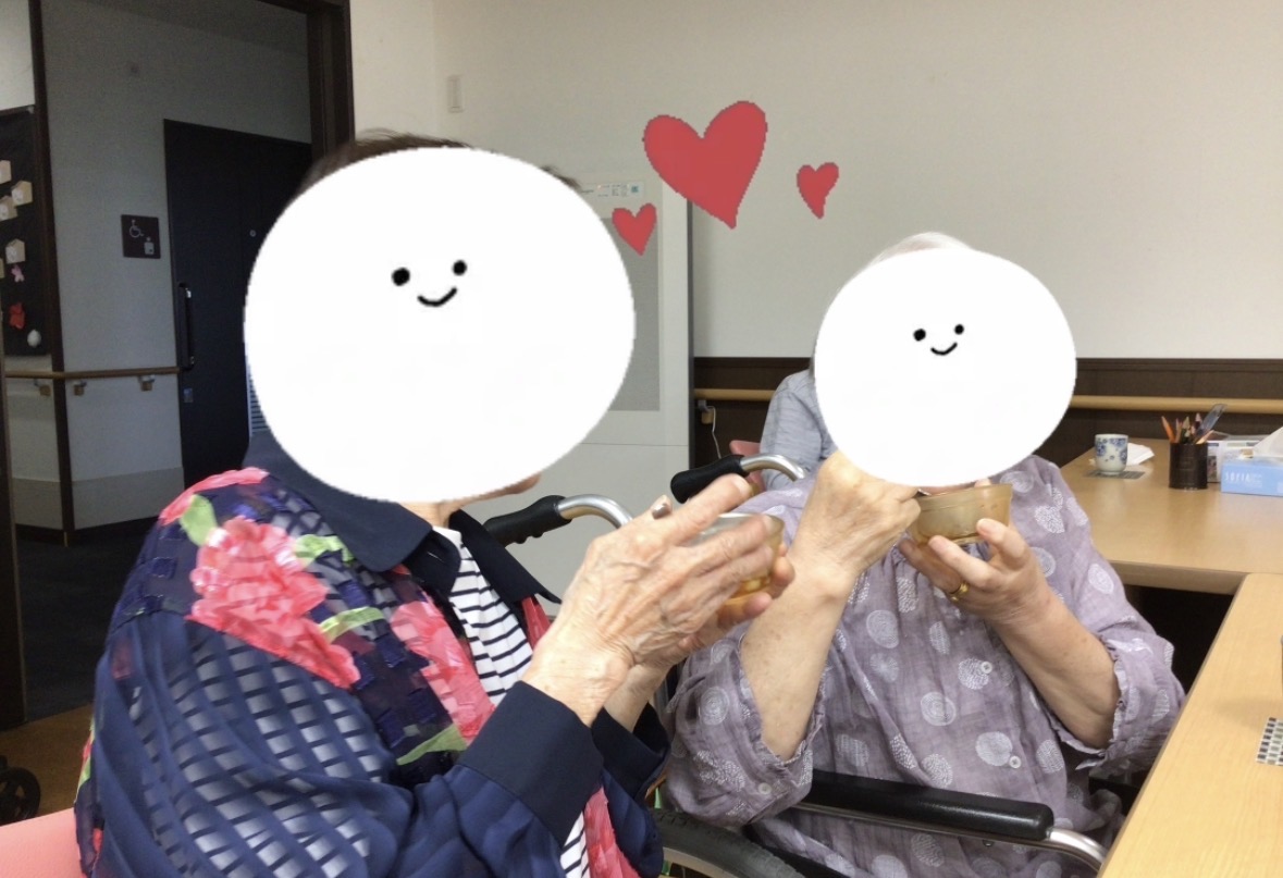 入居者が室内で手を繋いでいるレクリエーション風景。壁には赤いハートの装飾がある。